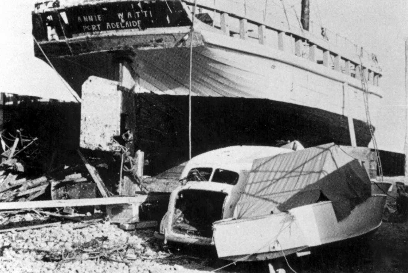 This image shows vessel on land from rear angle, showing rudder, and has an old car in foreground.