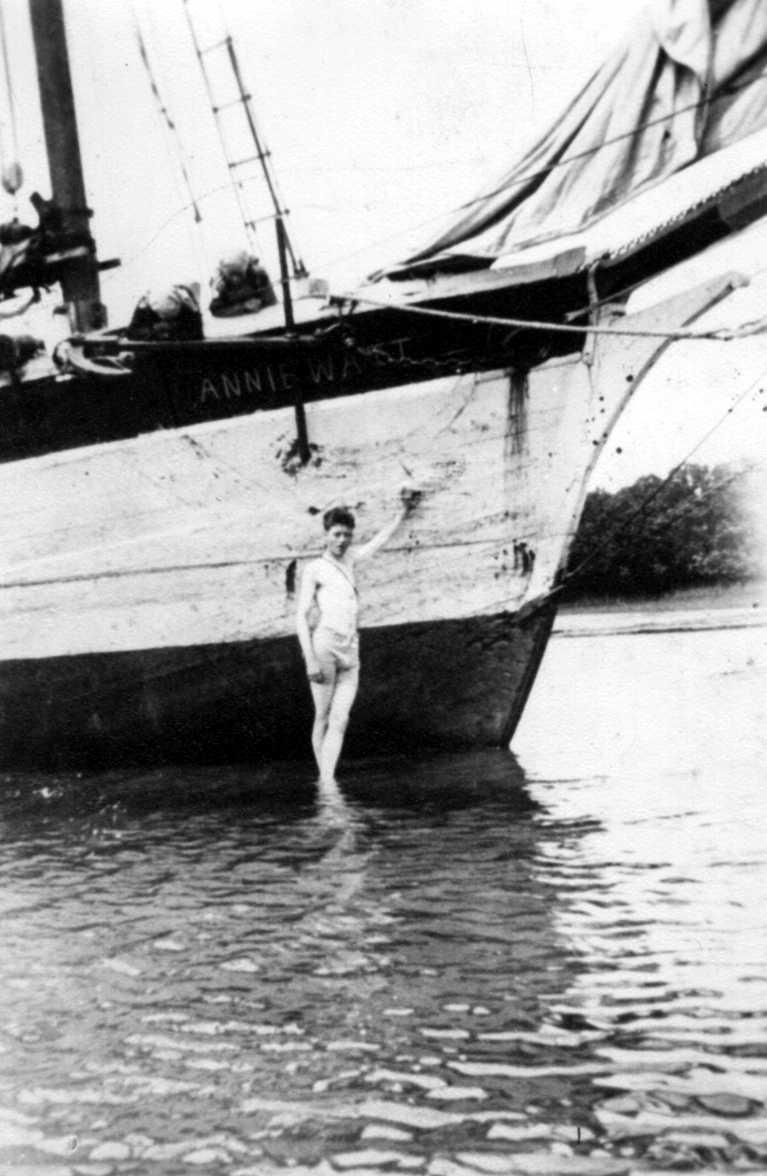 This image shows front of vessel in water with a young man standing under name.