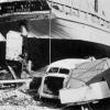 This image shows vessel on land from rear angle, showing rudder, and has an old car in foreground.